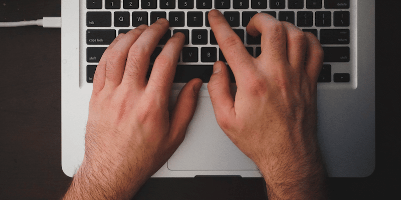 Hands typing on MacBook keyboard for gig economy job