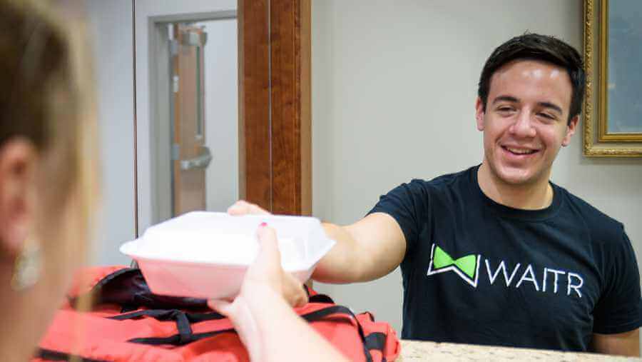 A waitr delivery driver handing a meal to a customer.