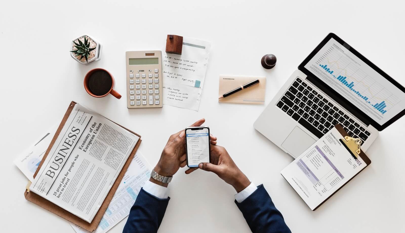 Businessman with cell phone, laptop, calculator, and newspaper