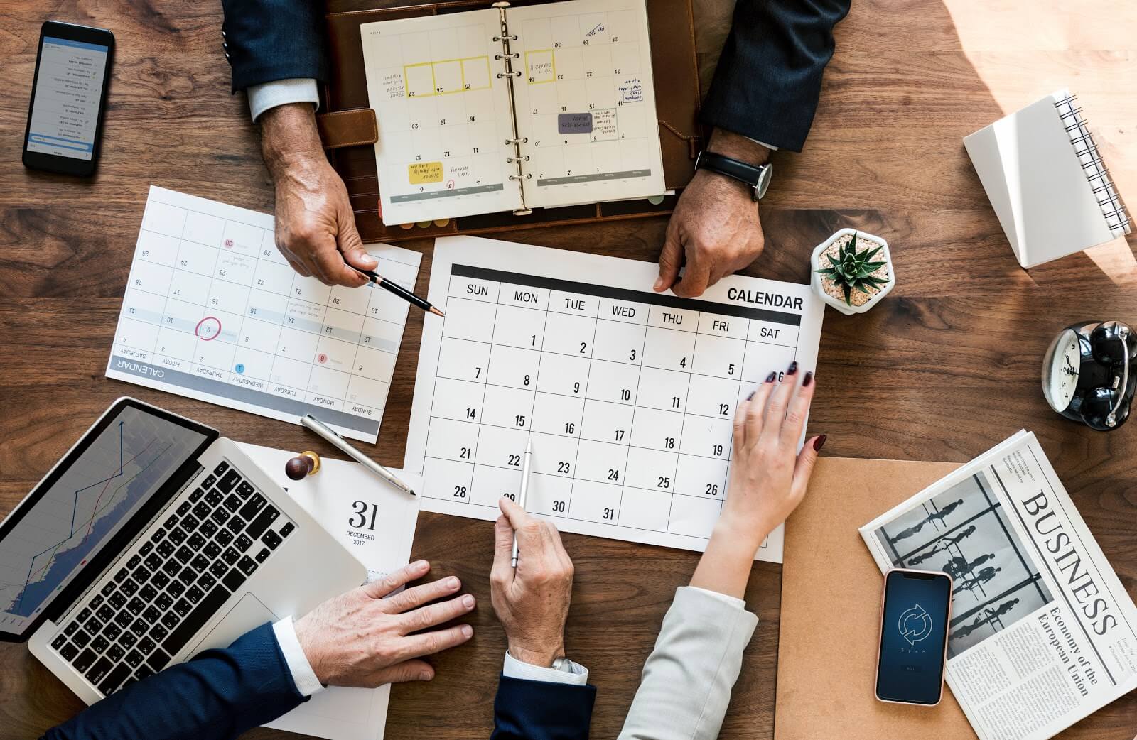 Professionals at a desk with calendars, cell phones, and laptop