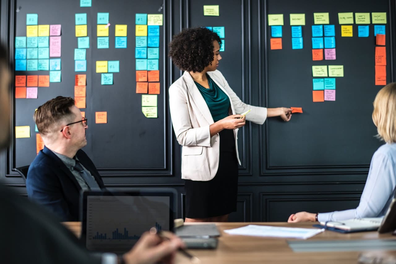 Management styles: Woman pulling a sticky note off a wall in a meeting