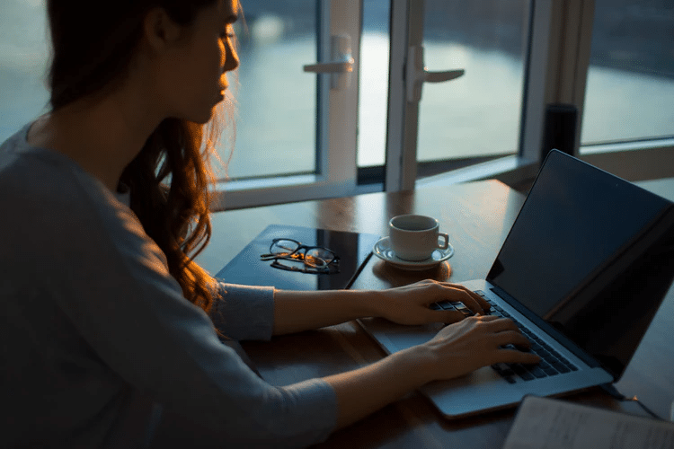 Woman typing on laptop with coffee next to her