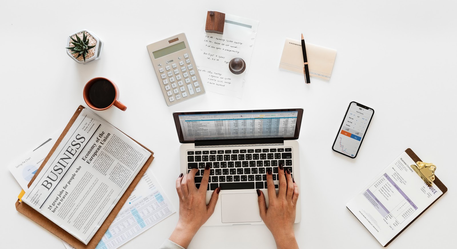 How to value a business: hands, laptop, newspaper, coffee cup, calculator, and clipboard on a desktop