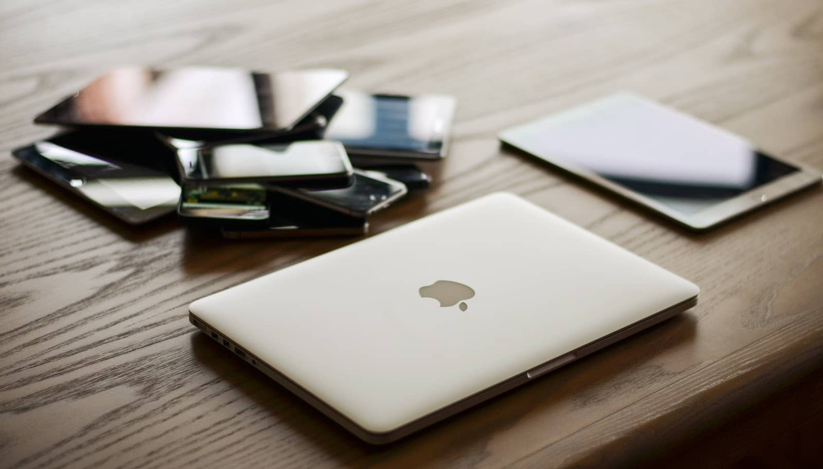 Wood table with a pile of phones, tablets, and a Mac laptop in the forefront