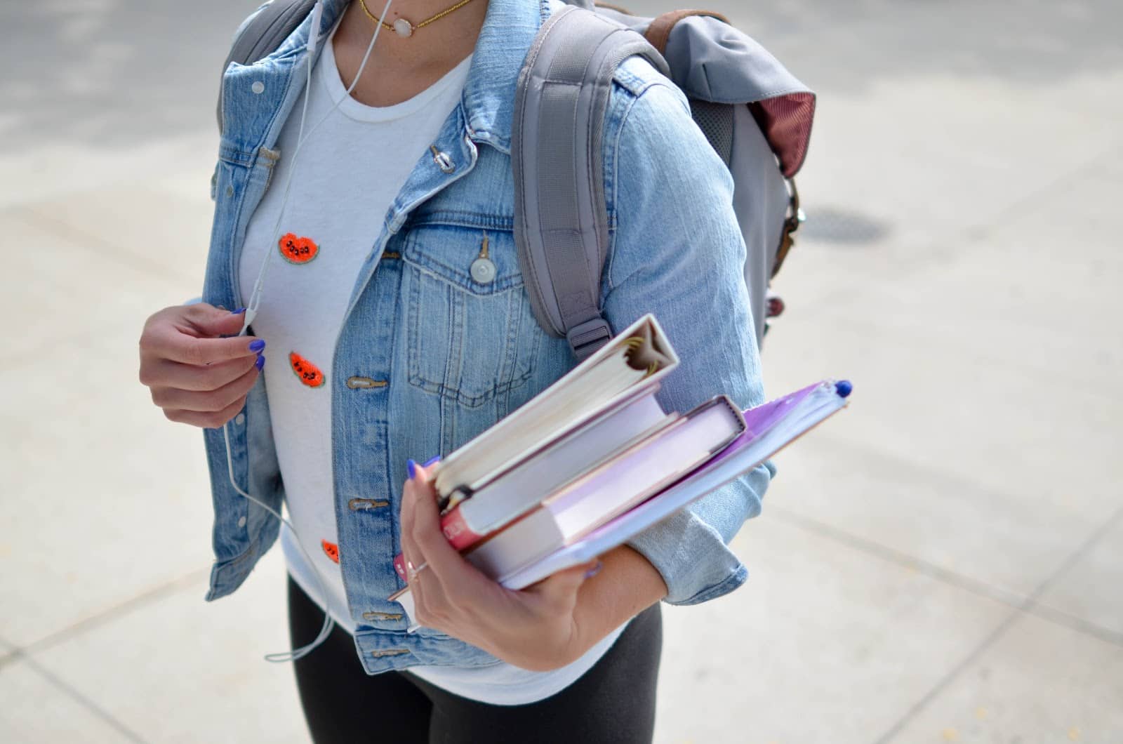 girl walking on campus with backpack and stack of books