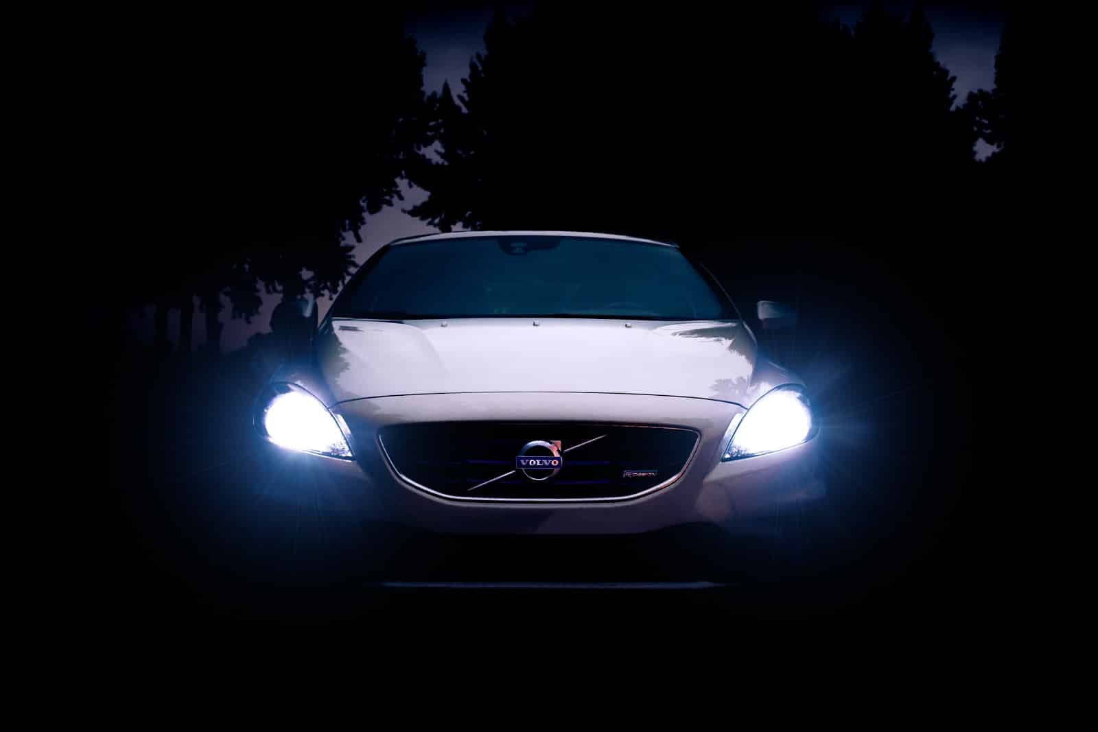 volvo headlights shining through trees at night