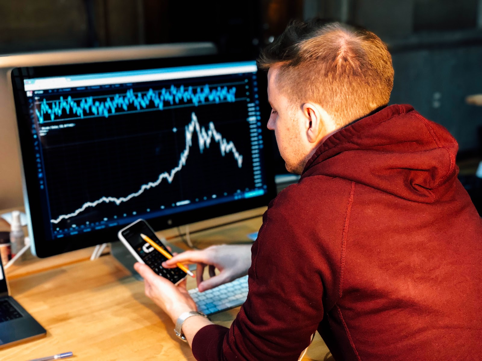 Is bitcoin a good investment: man looking at phone with chart on desktop screen