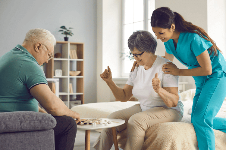 A supportive caregiver watching a senior couple playing together in the living room
