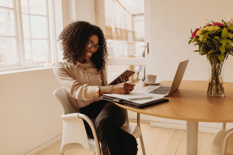 A cheerful young woman taking notes and working on a wooden table