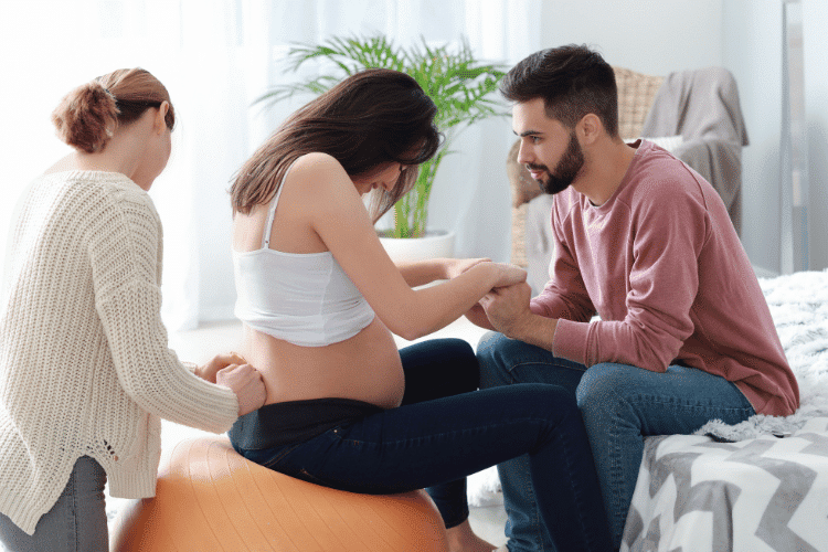 A doula working with a pregnant woman whose husband holding her hands in a bedroom