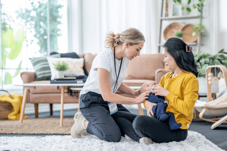 A female lactation consultant checking a sitting mother feeding her baby in a living room