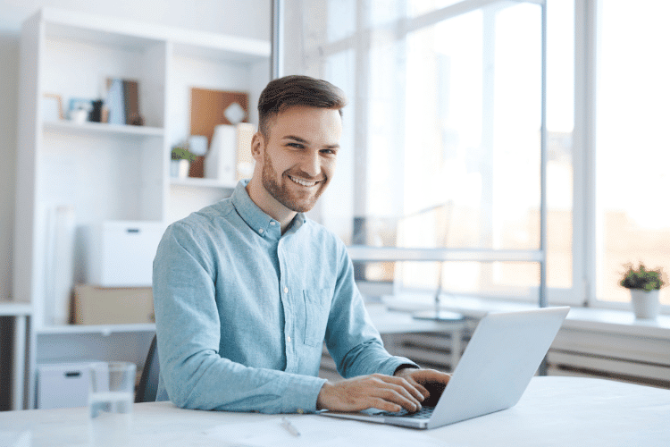 A smiling young man working on his laptop in the office