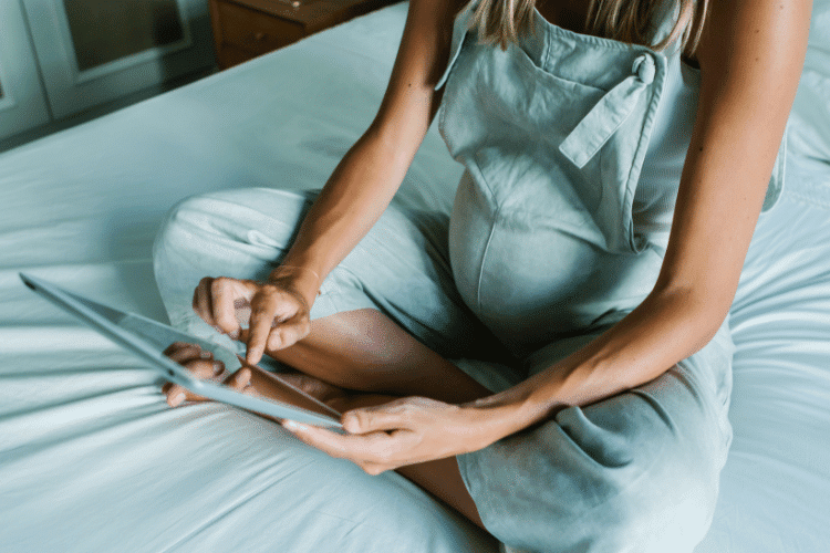 Pregnant Woman in Jumper Sitting on Bed and Using Tablet
