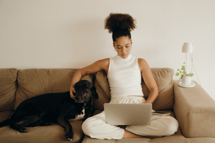 Woman with Dog Working on a Laptop on the Sofa
